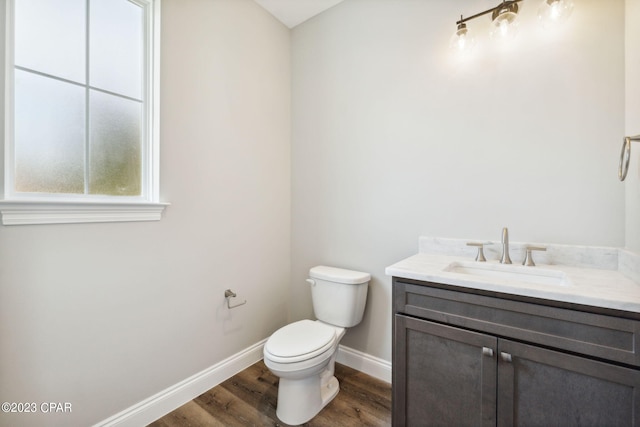 half bathroom with toilet, vanity, baseboards, and wood finished floors