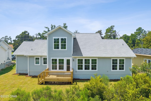 rear view of property with roof with shingles, a deck, and a yard