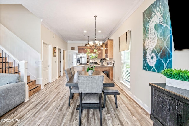 dining space featuring light wood-style floors, crown molding, baseboards, a chandelier, and stairs