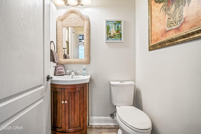 half bathroom featuring baseboards, toilet, wood finished floors, and vanity