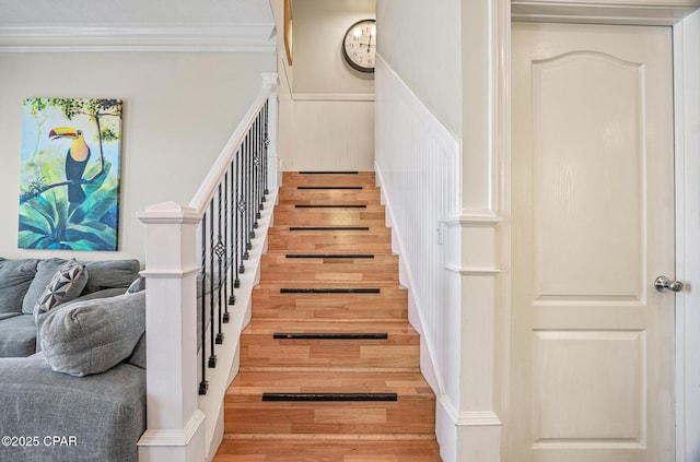 stairway with wood finished floors, a wainscoted wall, and ornamental molding