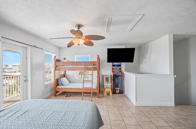 bedroom with attic access, wainscoting, tile patterned flooring, access to exterior, and a textured ceiling