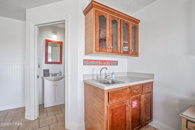 bar featuring a wainscoted wall, a textured ceiling, and a sink