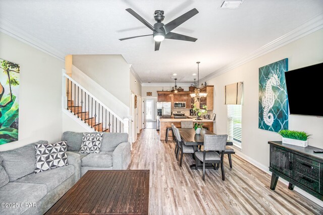 living room with visible vents, crown molding, ceiling fan, stairway, and light wood-style flooring