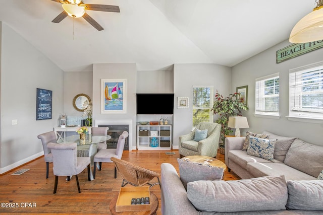 living room with visible vents, wood finished floors, baseboards, ceiling fan, and vaulted ceiling