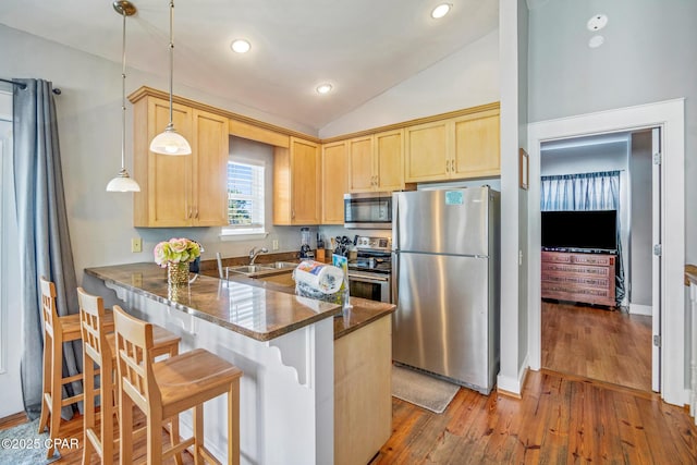 kitchen featuring light brown cabinetry, vaulted ceiling, a peninsula, stainless steel appliances, and a sink