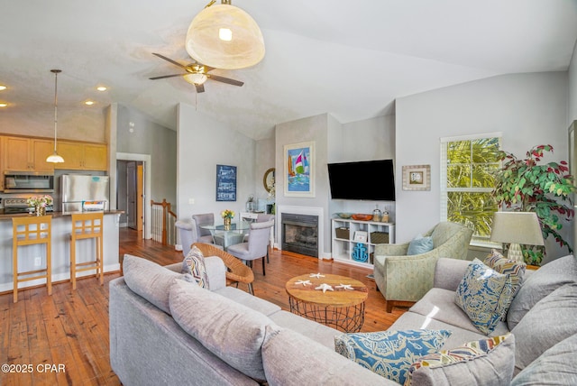 living room featuring hardwood / wood-style floors, baseboards, high vaulted ceiling, a fireplace, and ceiling fan