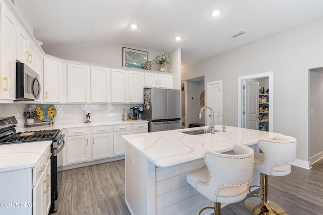 kitchen with a sink, tasteful backsplash, white cabinetry, stainless steel appliances, and lofted ceiling