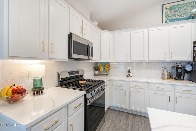 kitchen featuring light wood-type flooring, stainless steel appliances, white cabinets, decorative backsplash, and lofted ceiling