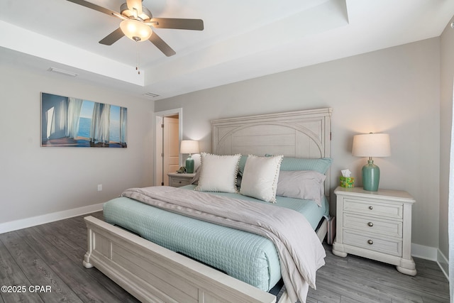 bedroom with a tray ceiling, wood finished floors, baseboards, and ceiling fan