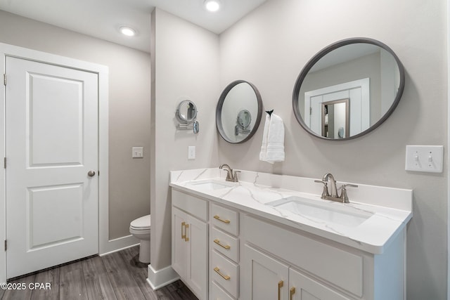 full bath with double vanity, toilet, wood finished floors, and a sink