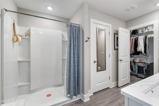 full bathroom with visible vents, wood finished floors, a walk in closet, and a stall shower