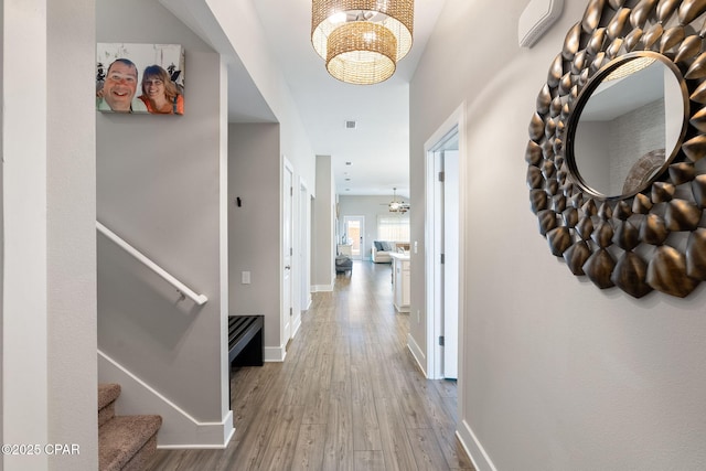 hallway featuring baseboards, an inviting chandelier, wood finished floors, and stairs