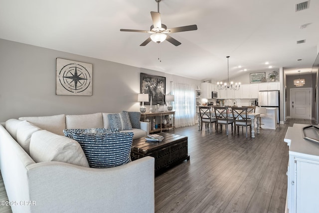 living area with visible vents, ceiling fan with notable chandelier, wood finished floors, and vaulted ceiling