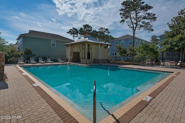 community pool with an outdoor structure, a patio area, and fence