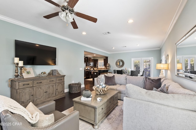 living room with light wood-style flooring, a ceiling fan, visible vents, and ornamental molding
