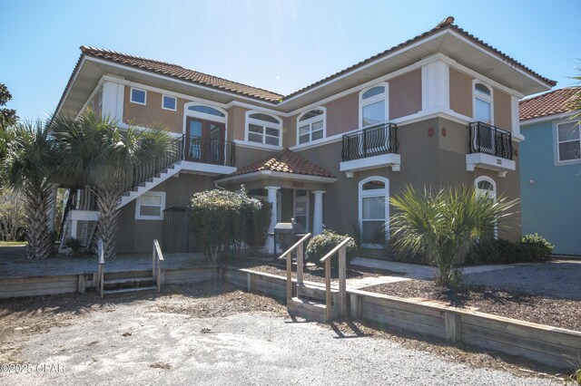 mediterranean / spanish house featuring stucco siding, a tiled roof, and a balcony