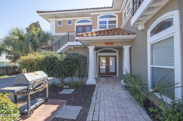 doorway to property with a tiled roof, stucco siding, french doors, and fence