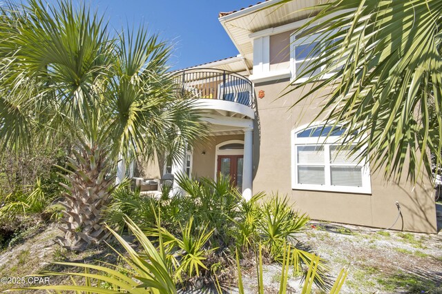 view of exterior entry featuring stucco siding, french doors, and a balcony