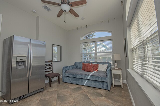 living area featuring visible vents, baseboards, ceiling fan, and a towering ceiling