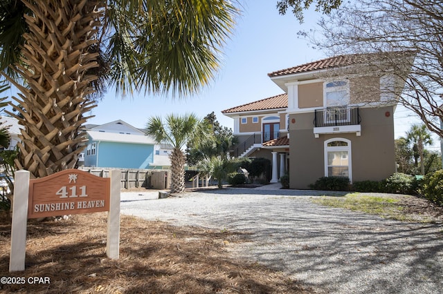 view of front of home featuring a balcony, fence, gravel driveway, stucco siding, and a tile roof