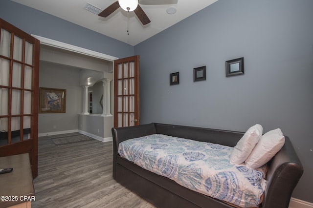 bedroom featuring decorative columns, wood finished floors, visible vents, and baseboards