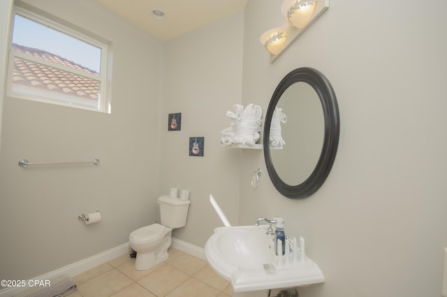 half bath with tile patterned floors, baseboards, toilet, and a sink