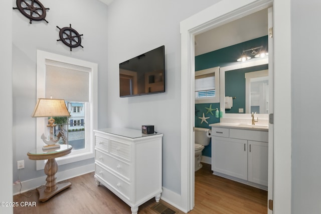 hall featuring visible vents, light wood-type flooring, baseboards, and a sink