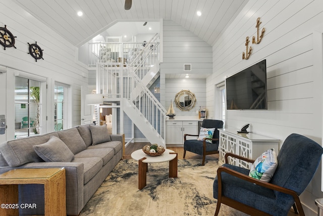 living room featuring stairway, high vaulted ceiling, wooden walls, and wood finished floors