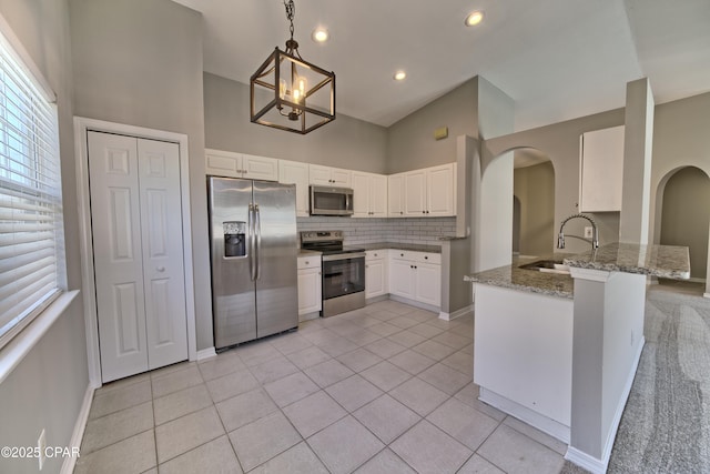 kitchen featuring tasteful backsplash, light stone counters, appliances with stainless steel finishes, arched walkways, and a sink