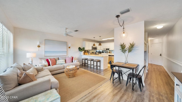 living room featuring visible vents, ceiling fan, and light wood finished floors