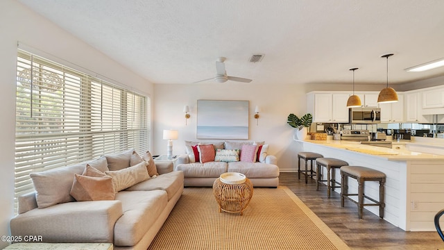 living room featuring visible vents, baseboards, ceiling fan, dark wood-style floors, and a textured ceiling