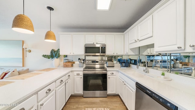 kitchen featuring light wood finished floors, light countertops, appliances with stainless steel finishes, white cabinetry, and decorative light fixtures