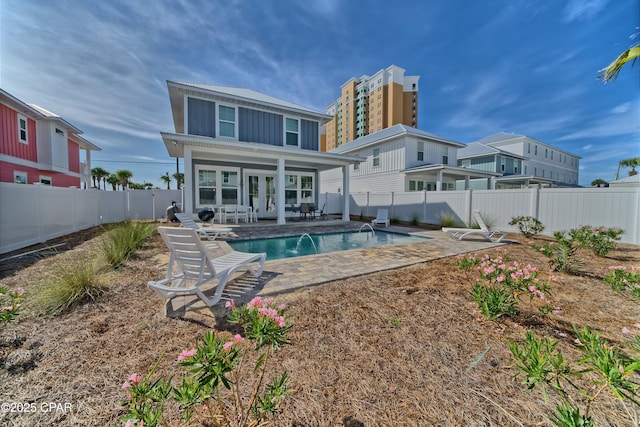 rear view of property featuring a fenced in pool, a fenced backyard, french doors, a patio area, and board and batten siding