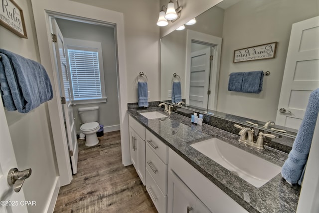 full bath with double vanity, toilet, wood finished floors, and a sink