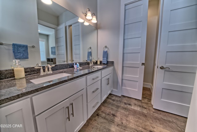 bathroom featuring double vanity, wood finished floors, baseboards, and a sink