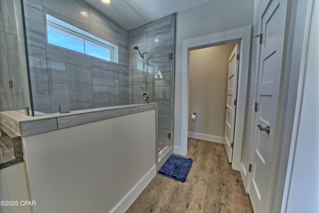 bathroom with baseboards, wood finished floors, and a tile shower