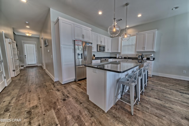 kitchen with stainless steel appliances, a kitchen island, dark wood-style flooring, and white cabinetry