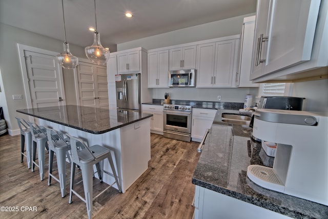 kitchen featuring dark wood-type flooring, dark stone countertops, a kitchen island, appliances with stainless steel finishes, and a breakfast bar area