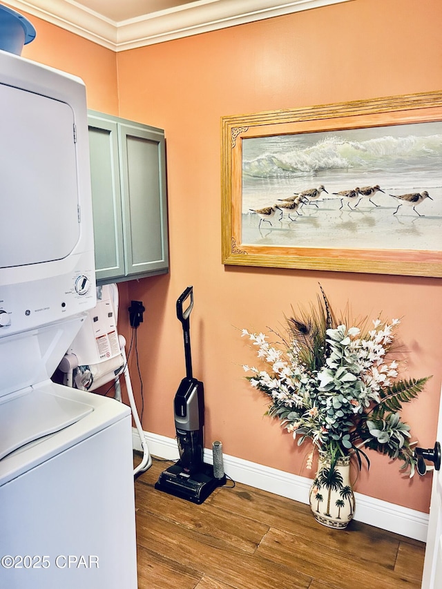 laundry room with cabinet space, stacked washing maching and dryer, baseboards, and wood finished floors