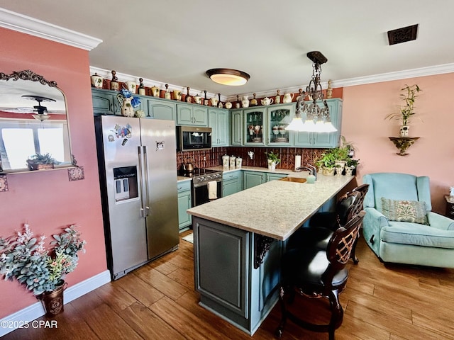 kitchen with a peninsula, ornamental molding, green cabinetry, and stainless steel appliances