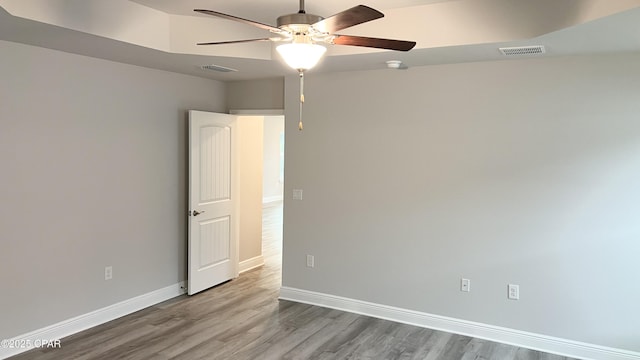 empty room with wood finished floors, a ceiling fan, visible vents, and baseboards