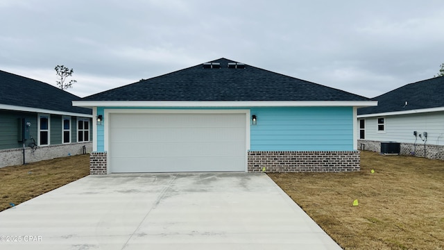 exterior space with an attached garage, roof with shingles, a lawn, cooling unit, and driveway