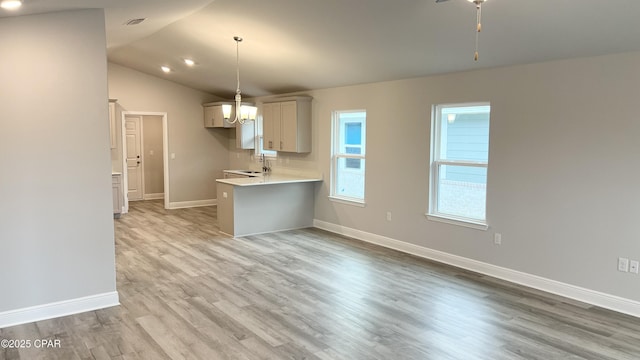 kitchen with a peninsula, light wood finished floors, baseboards, light countertops, and vaulted ceiling