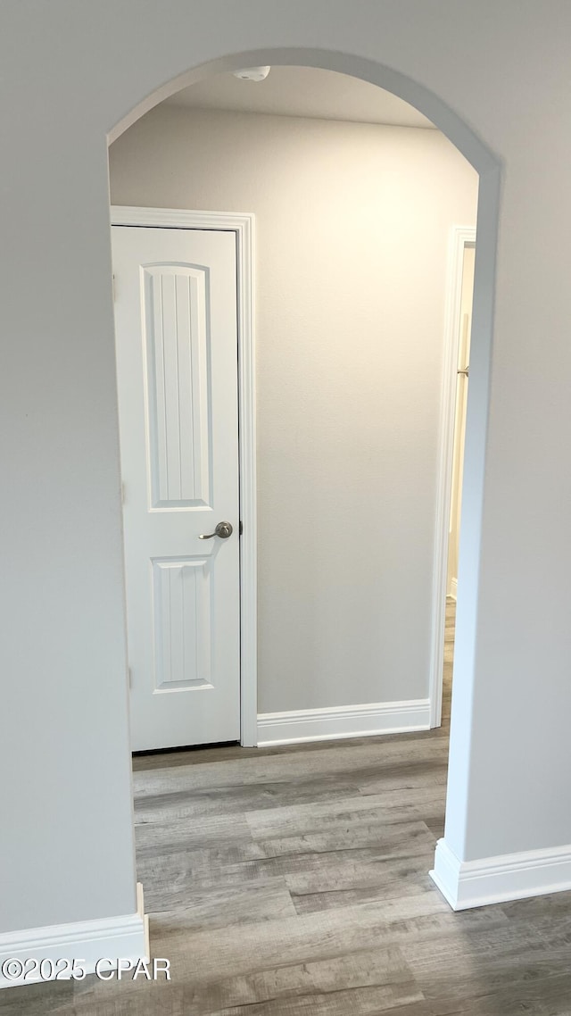 corridor featuring arched walkways, baseboards, and wood finished floors