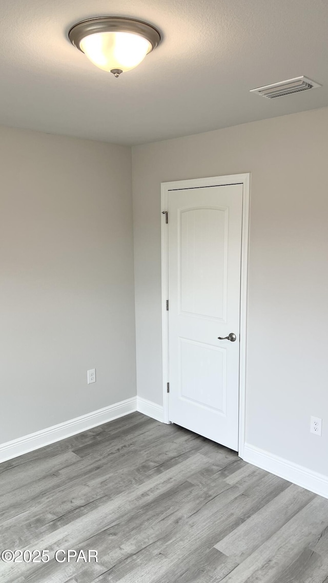 spare room featuring wood finished floors, visible vents, and baseboards