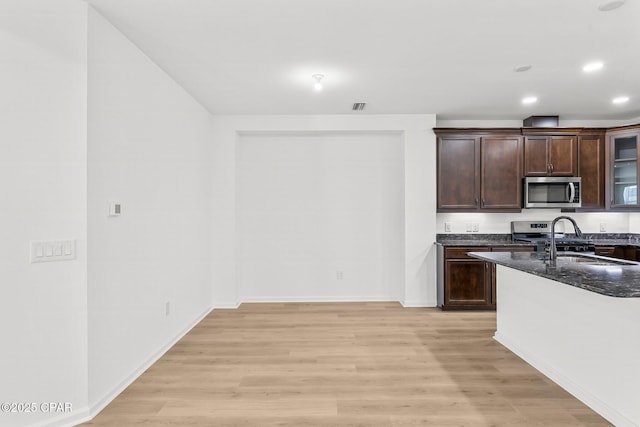 kitchen with light wood-type flooring, visible vents, dark stone countertops, stainless steel appliances, and dark brown cabinets