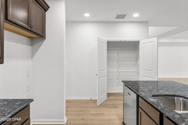 kitchen featuring visible vents, stainless steel dishwasher, dark stone counters, light wood-style floors, and dark brown cabinetry