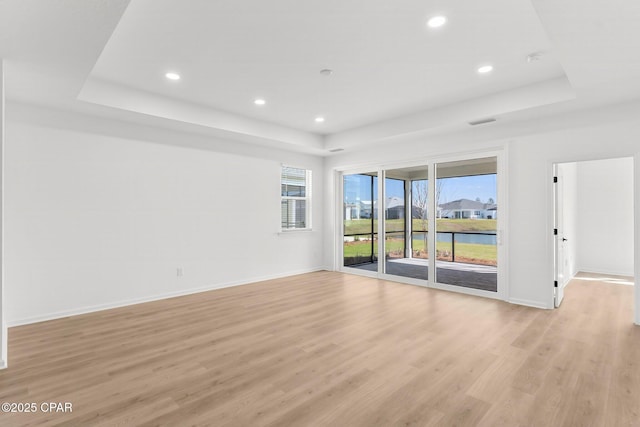 unfurnished room featuring plenty of natural light, light wood-style flooring, baseboards, and a tray ceiling