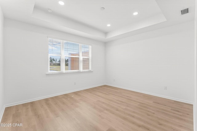 empty room featuring visible vents, recessed lighting, baseboards, light wood-style floors, and a raised ceiling